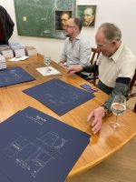 Mats Linder og Gerhard Berg sitter ved et bord. Berg signerer postere
